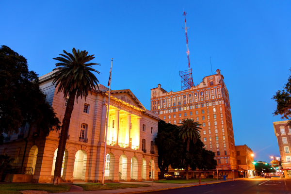 Historic building with columns lit warmly at dusk, palm trees lining a quiet city street.